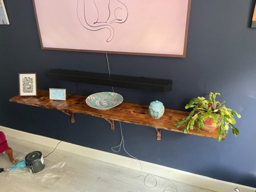 Wooden shelf against a dark wall, displaying a bowl, a plant, and decorative items.