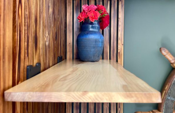 Wooden shelf with a blue vase holding pink flowers against a textured background.