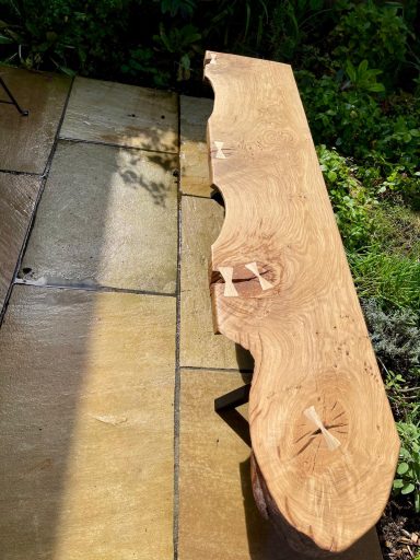 A rustic wooden bench with natural edges, placed on a stone patio.