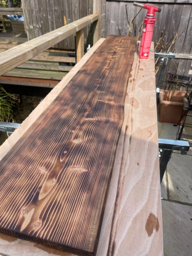 A wooden plank with a dark finish placed on a workbench, alongside a red tool.