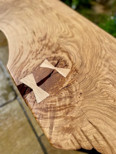 Two wooden butterflies set into a natural wood surface with grain patterns.