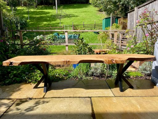 A rustic wooden table with a live edge, supported by black metal stands.