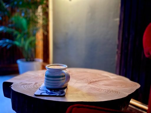 A ceramic mug on a wooden table with a plant in the background.