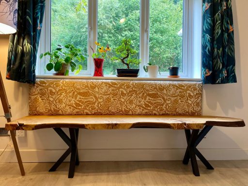 A wooden bench by a window with potted plants and patterned curtains.