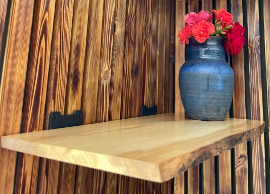 Wooden shelf with a blue vase and red flowers against a wooden backdrop.
