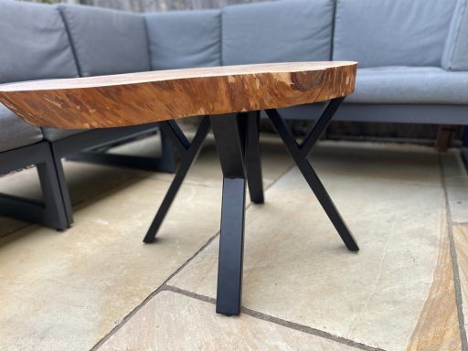 Wooden coffee table with a live edge top and black metal legs, set on a patio.
