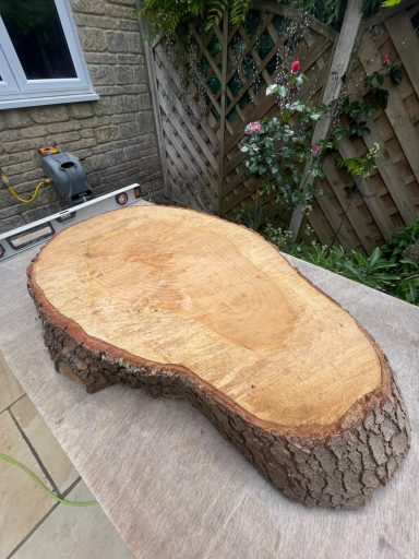 Smooth, polished wooden slab with a natural edge, placed on a table outside.