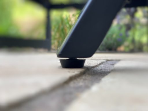 Close-up of a chair leg resting on a patio with uneven stones and grass nearby.